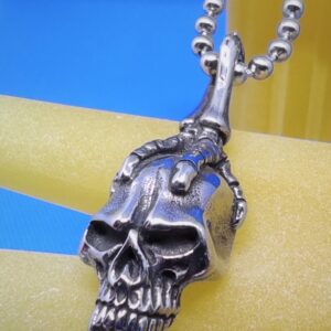 Pendentif gothique acier griffe squelette tenant une tête de mort, style gothique rock biker punk